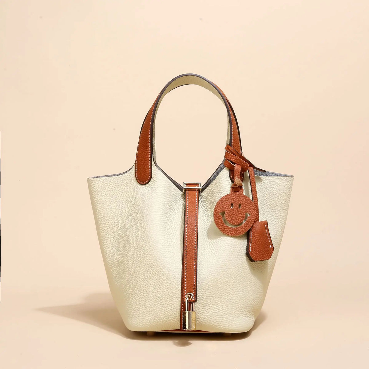 Beige Leder-Bucketbag mit braunen Ledergriffen und Zierleisten, vor hellem Hintergrund.