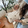 A beige corduroy clutch bag is held by a person, set against a bright indoor background.