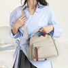A woman wearing a light blue striped shirt carries a beige multi-pocket shoulder crossbody bag.
