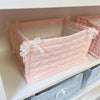 Pink quilted cotton storage basket with white lace flower design resting on a shelf.