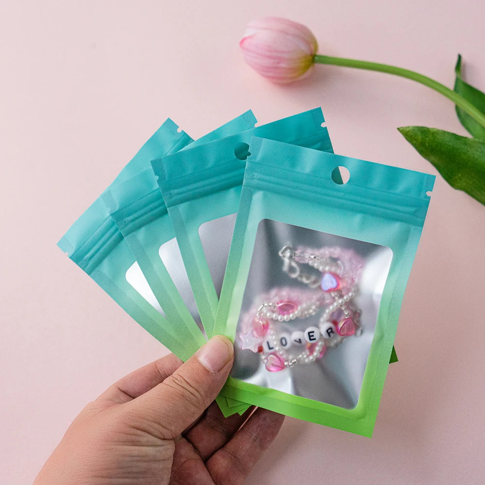 A hand holds a clear plastic bag filled with pink and white pearl jewelry inside a teal resealable storage bag.