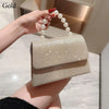 Una mano sostiene un bolso de fiesta beige con lazo brillante y detalles de perlas.