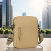 Sac bandoulière beige unisexe posé sur une surface claire avec des bâtiments de ville flous en arrière-plan.