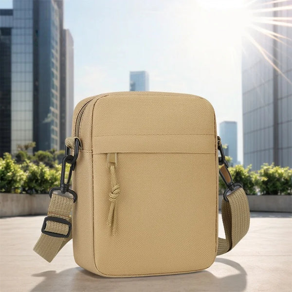 Sac bandoulière beige unisexe posé sur une surface claire avec des bâtiments de ville flous en arrière-plan.
