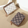 A pair of zippered card holder wallets, one white and one dark brown, resting on a beige surface.