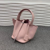 Helle rosa Leder-Bucketbag mit Schnurverschluss auf grauer Oberfläche.