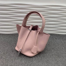 Sac bucket en cuir véritable rose pâle avec fermeture à cordon sur une surface grise.