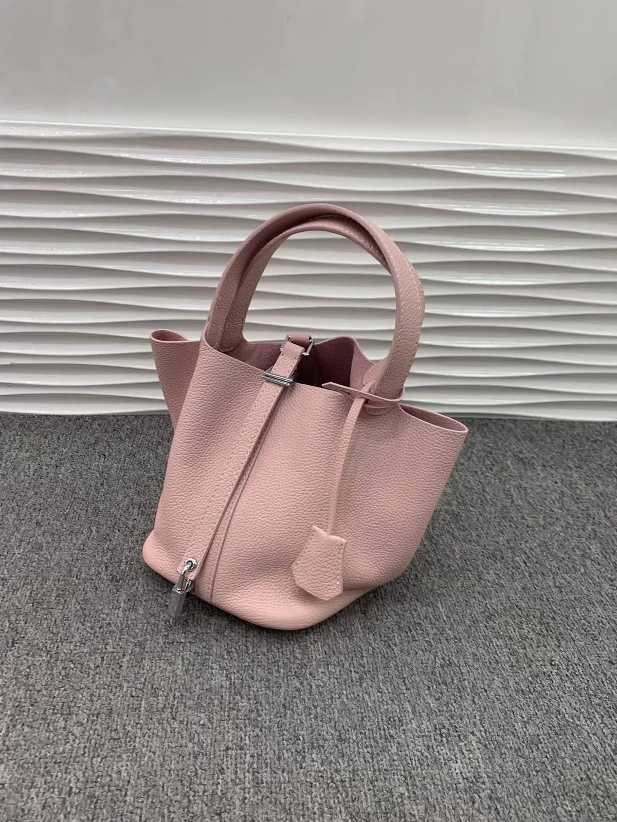 Helle rosa Leder-Bucketbag mit Schnurverschluss auf grauer Oberfläche.