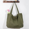 A large olive green canvas shoulder tote bag hanging against a white wall with pink tulips.