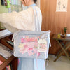 A light gray transparent shoulder tote bag decorated with pink and pastel fabric charms and a cream knit sweater.