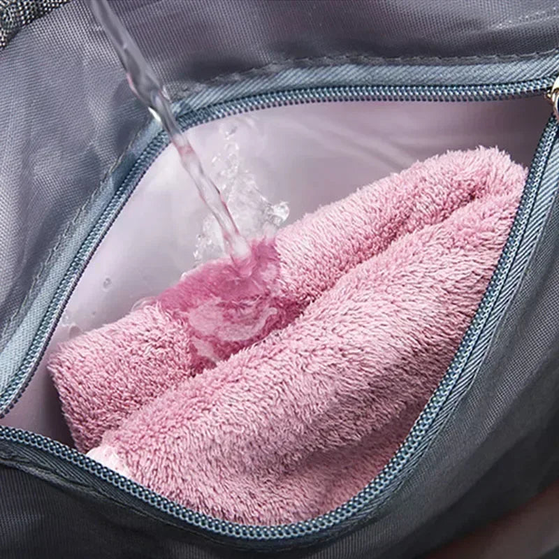 A pink towel is being rinsed with water inside a gray travel duffle bag.