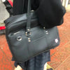A black women's Japanese style PU shoulder bag with a flap and strap is shown against a reddish-brown tiled background.