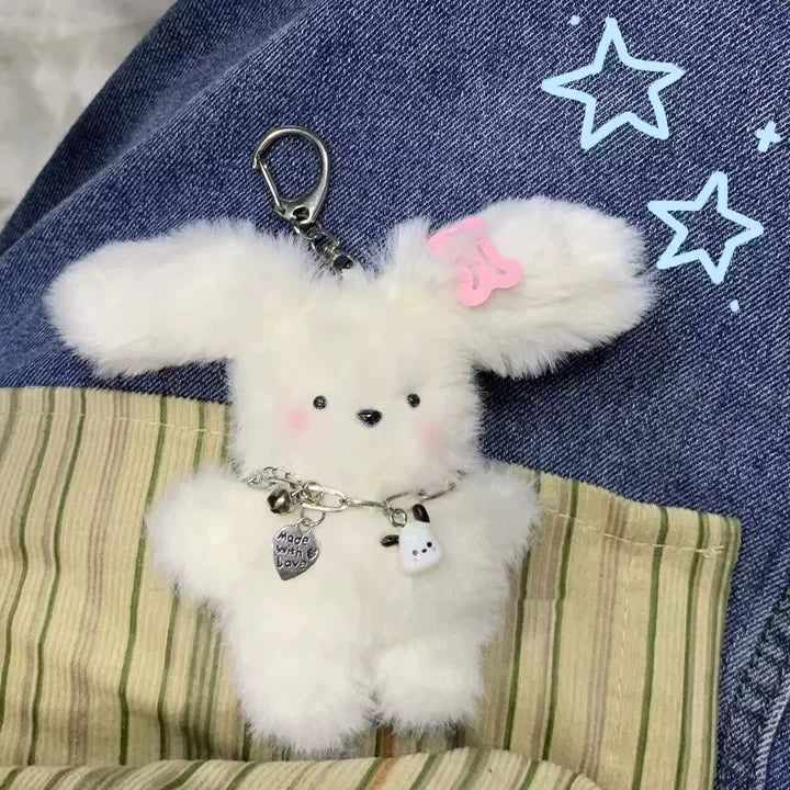 A fluffy white bunny charm attached to a silver chain is displayed against a denim background.