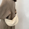 A beige women's preppy sling crossbody bag is shown hanging from a tan coat.