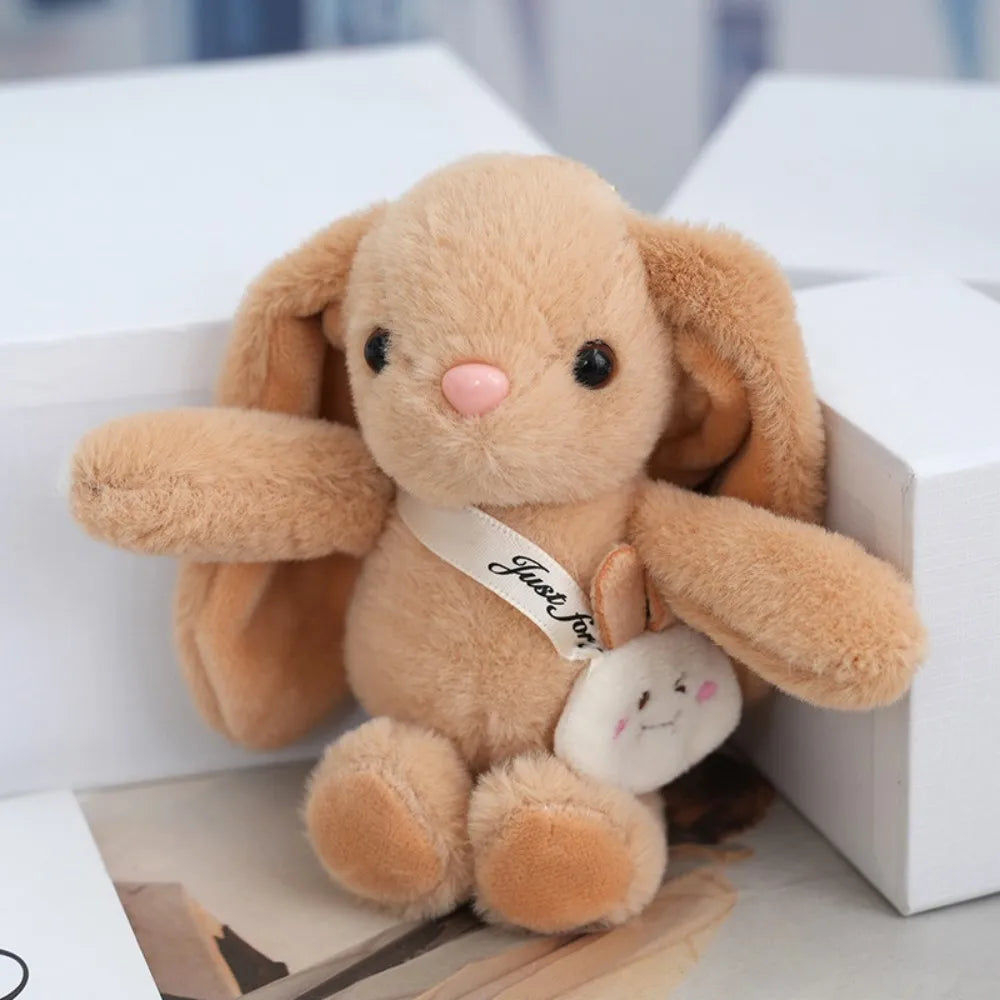 A fluffy light brown plush rabbit toy with pink accents sitting next to a white tag.