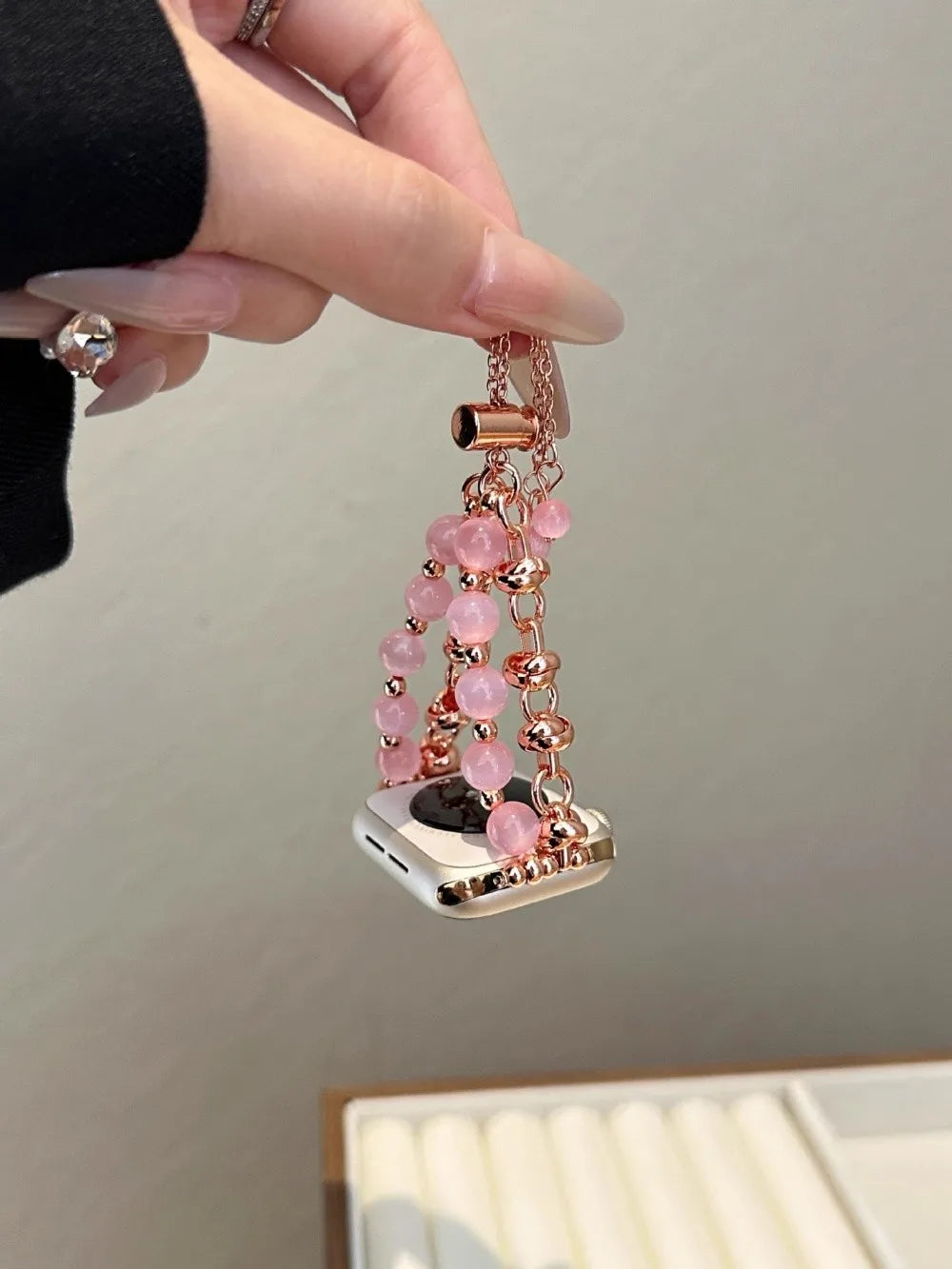 Eine Hand hält ein verstellbares Metallarmband mit rosa Kristallperlen und einem silberfarbenen Anhänger.