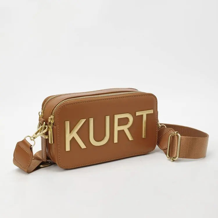 A brown leather pouch or bag with the name KURT embossed in gold lettering and a tan strap.