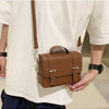 A man wearing a white t-shirt holds a brown leather minimalist crossbody bag.