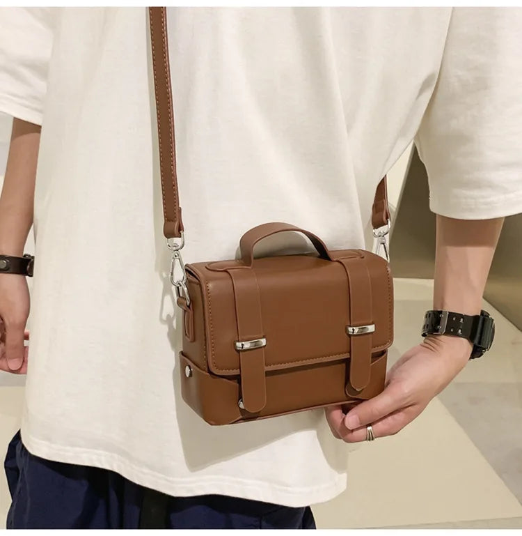 A man wearing a white t-shirt holds a brown leather minimalist crossbody bag.