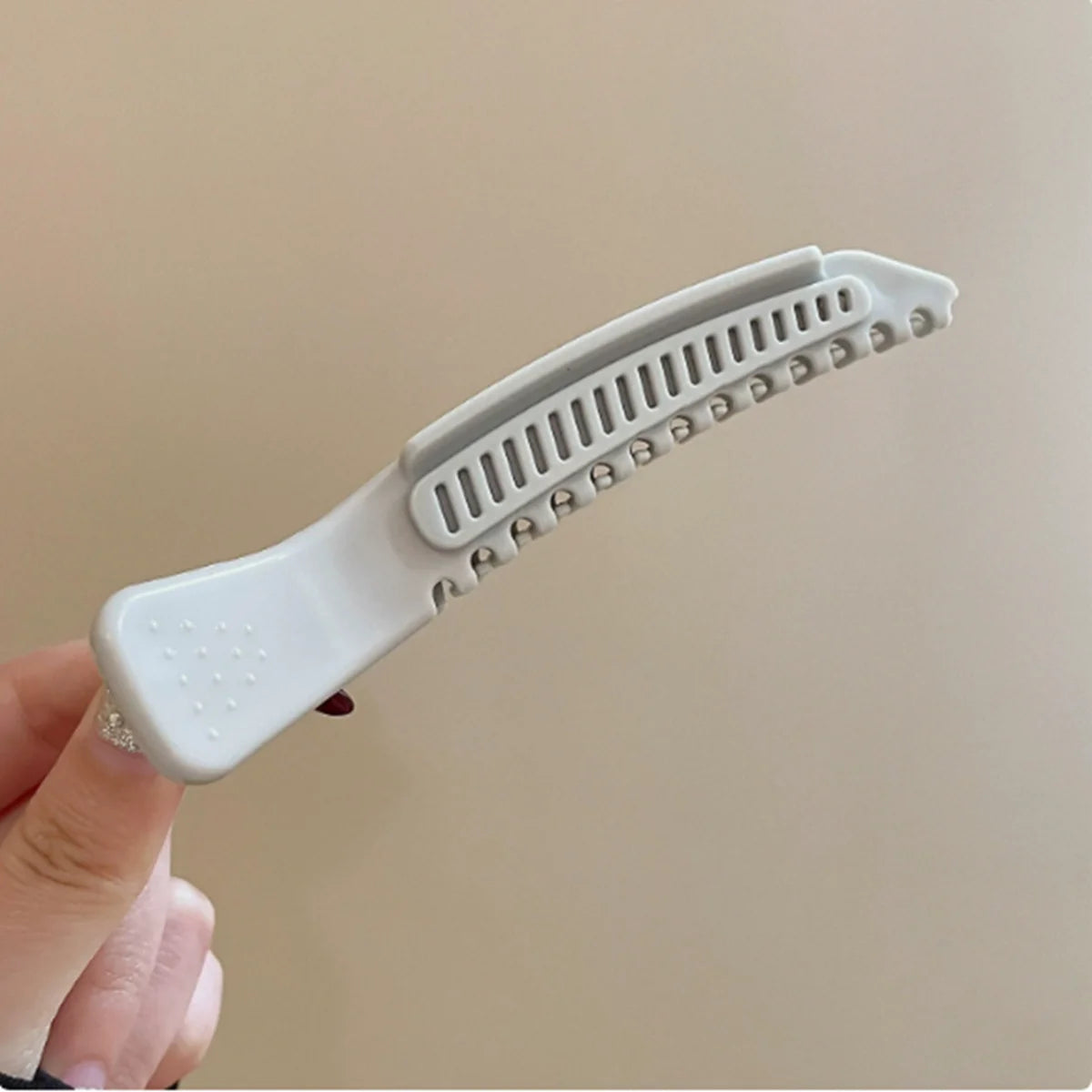 Une main tient une pince à cheveux blanche professionnelle antidérapante avec des textures et un anneau décoratif.