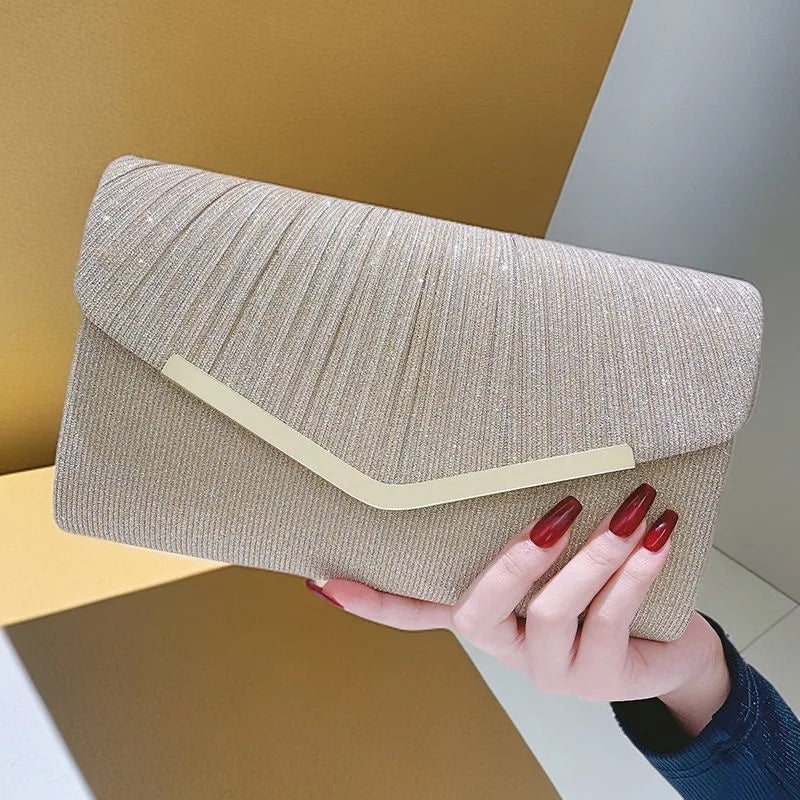 A hand holds a beige glitter pleated crossbody clutch bag against a light wall.