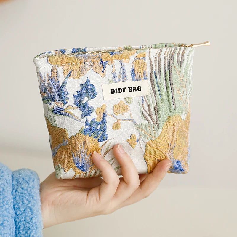 A hand holds a floral canvas makeup bag featuring blue and yellow botanical prints.