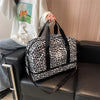 A black and white leopard print nylon travel duffle bag is being held by a person in a light-colored sweatshirt.