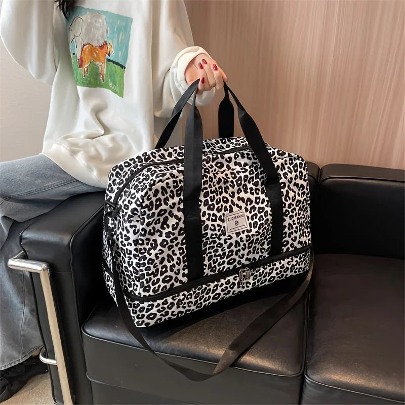 A black and white leopard print nylon travel duffle bag is being held by a person in a light-colored sweatshirt.