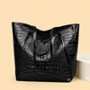 A black crocodile print tote bag is displayed on a light background.
