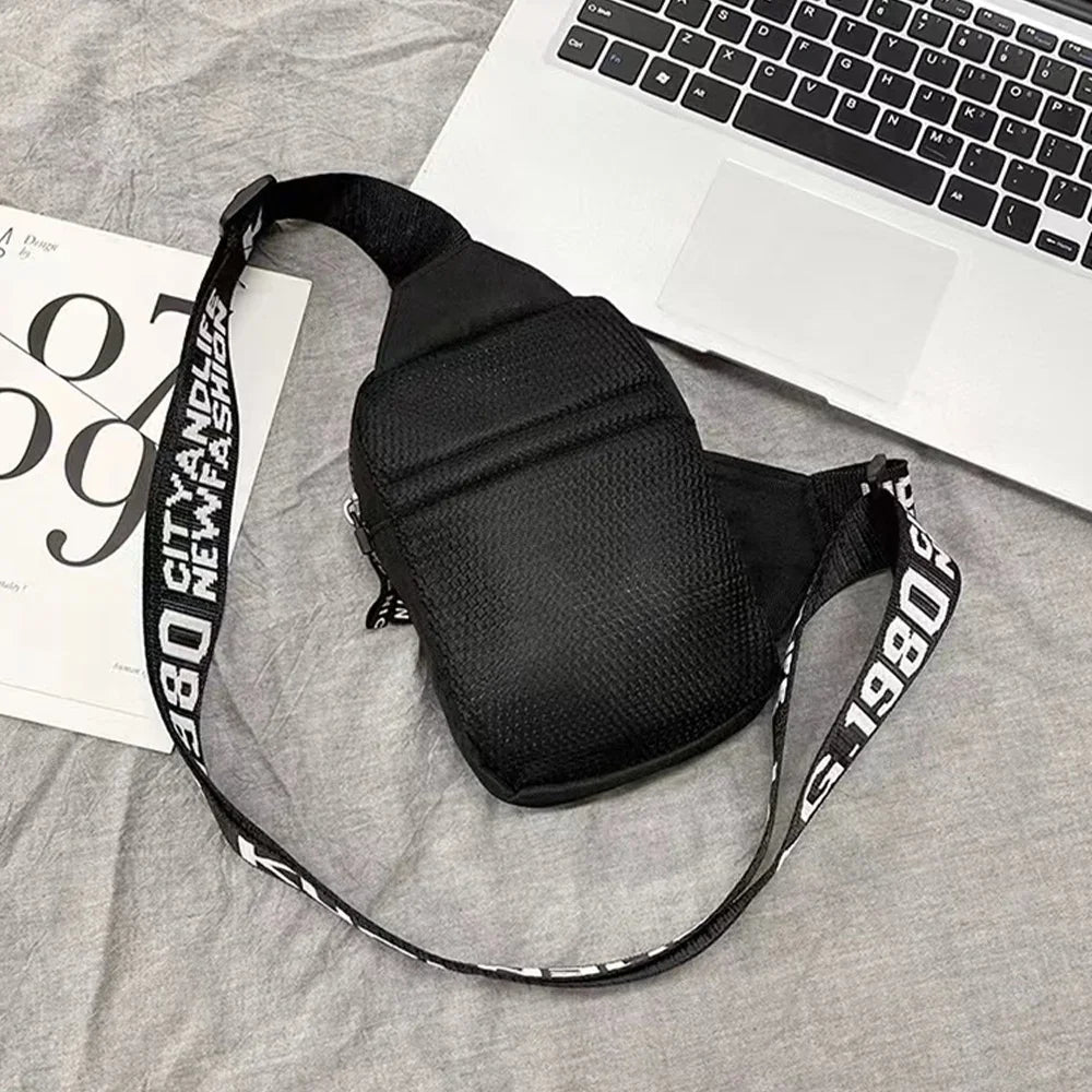 Schwarze multifunktionale Leinwandtasche mit weißer Beschriftung liegt auf grauem Stoff neben einem Laptop.