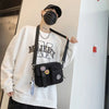 A person wearing a black face mask and a white sweatshirt holds a black canvas shoulder bag.