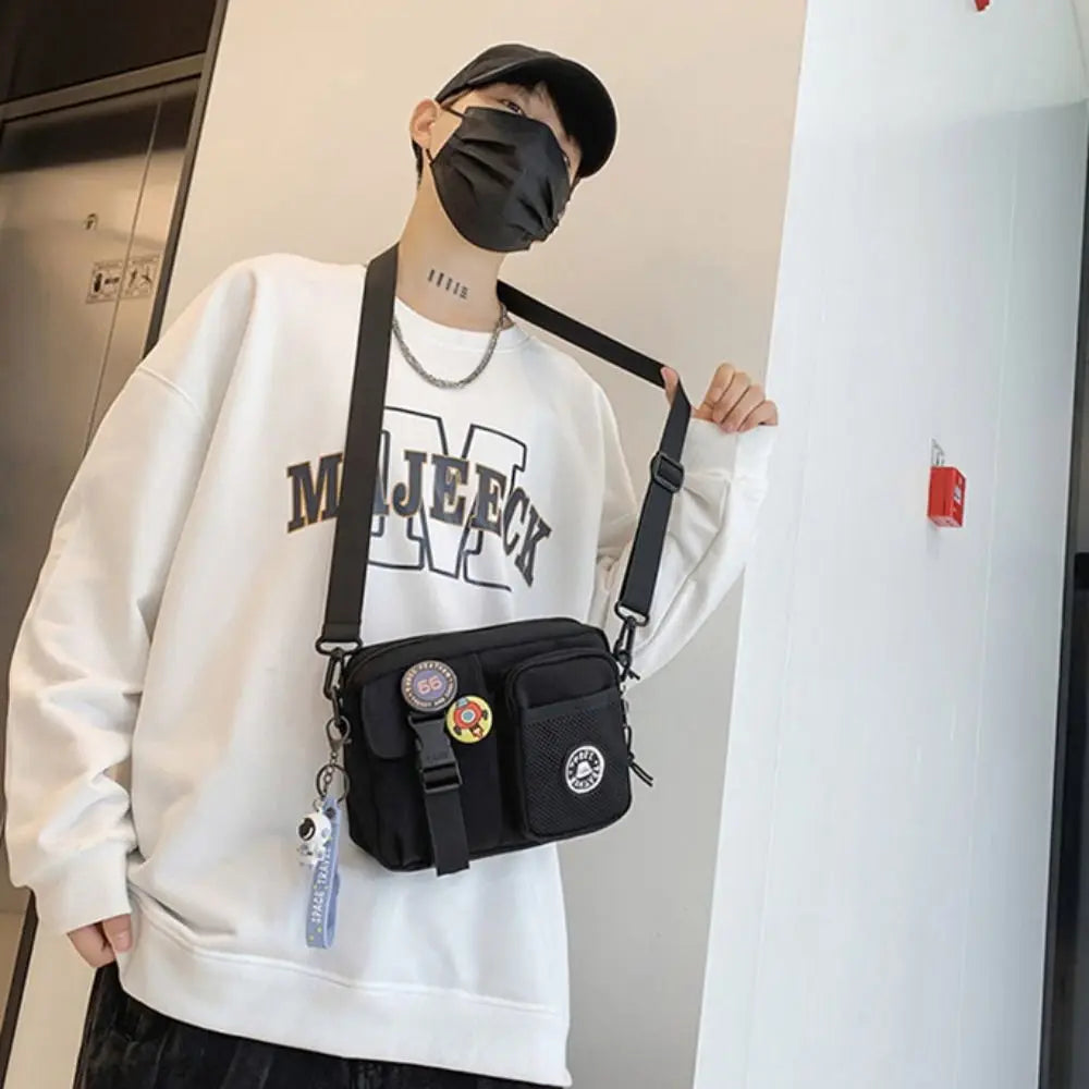 A person wearing a black face mask and a white sweatshirt holds a black canvas shoulder bag.