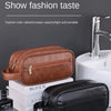 A brown leather wash bag and a black leather cosmetic pouch are displayed on a gray surface.