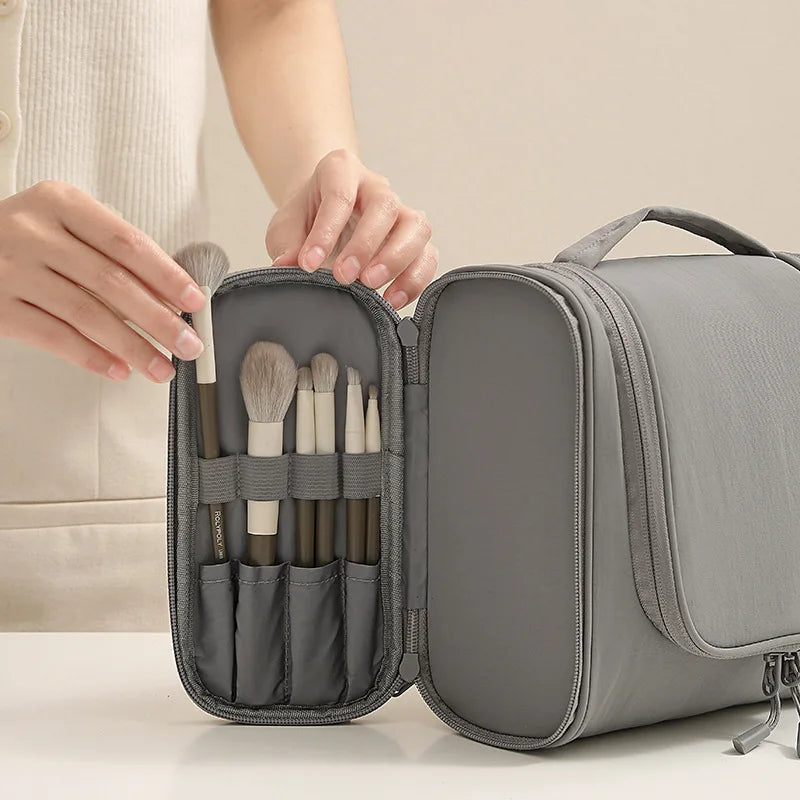 A gray waterproof hanging toiletry bag is shown open, revealing several brushes inside.