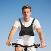 A man wearing a white shirt and shorts is riding a bicycle with a black tactical chest bag on the handlebars.