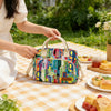 A woman holds a colorful patterned thermal storage bag on a checkered cloth outdoors.
