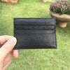 Ein schwarzes, echtes Kuhfell-ID-Card-Halter-Wallet wird in einer Hand vor einem unscharfen grünen Außenhintergrund gehalten.