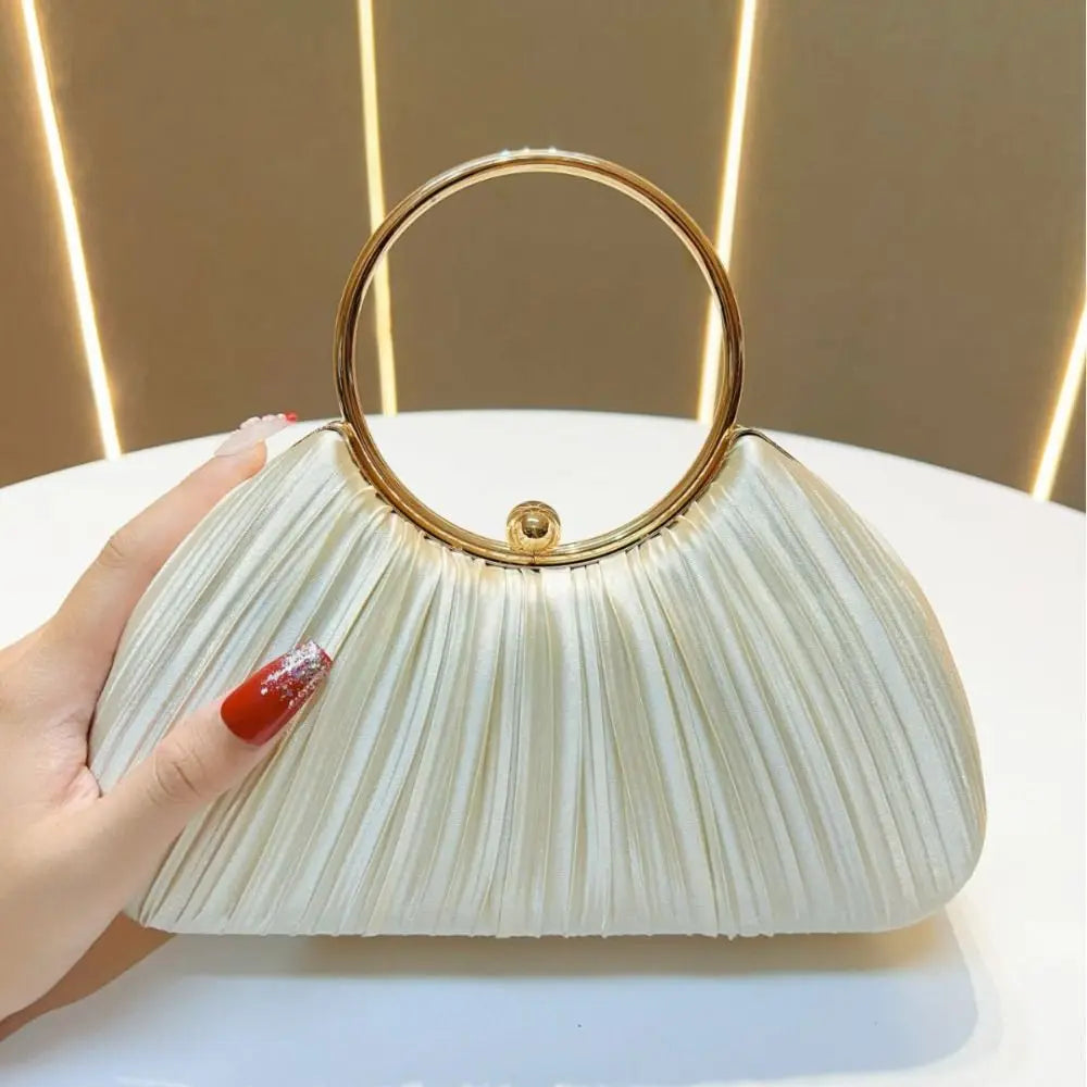 A hand holds an elegant satin pleated evening clutch bag with a gold rim against a light background.