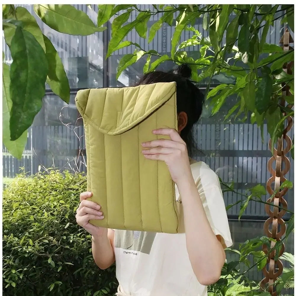 A person holds a lime green embroidered cotton laptop sleeve outdoors amidst lush green foliage.