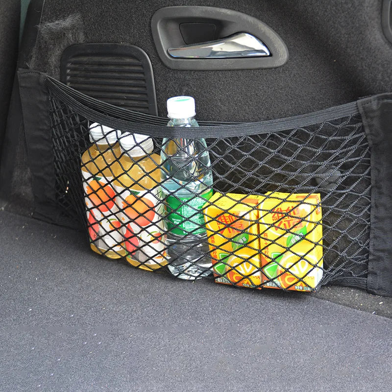 A black mesh storage net bag filled with various colorful snacks and a water bottle placed in a car trunk.