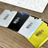 Three colored RFID blocking card sleeves placed on a wooden desk next to a white computer keyboard.