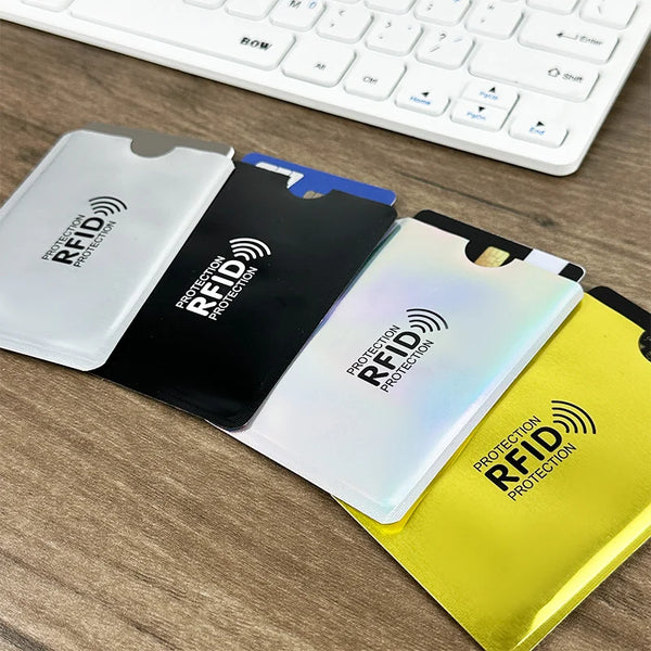 Three colored RFID blocking card sleeves placed on a wooden desk next to a white computer keyboard.