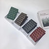 A collection of four geometric print passport wallets in various shades of green and brown displayed in their packaging.