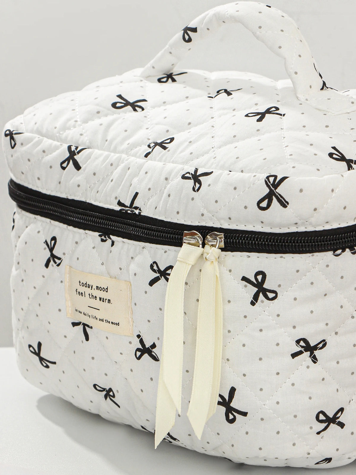 White quilted makeup bag with black ribbon details and a black zipper.