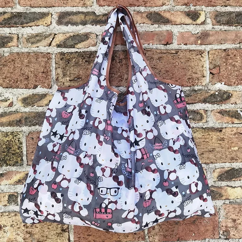 A reusable shopping bag featuring a pattern of cute white cats on a gray background, displayed against a brick wall.