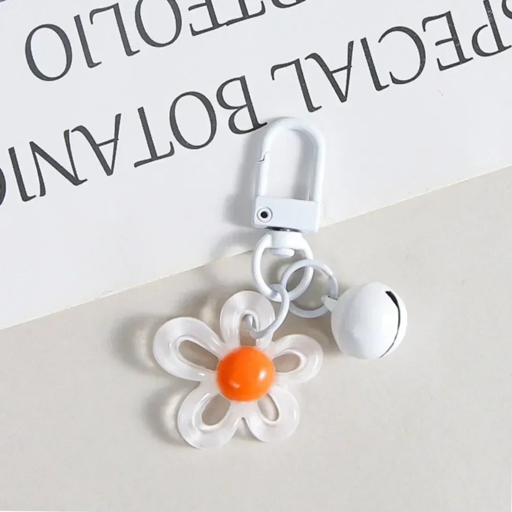 A white metal keychain featuring a clear resin flower charm with an orange center.