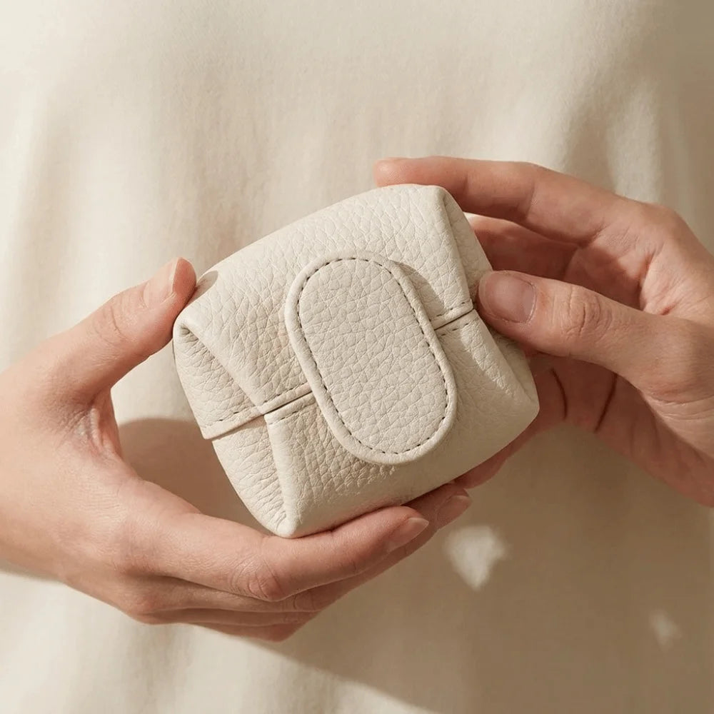A hand holds a light beige, lychee-textured coin purse with a snap closure.