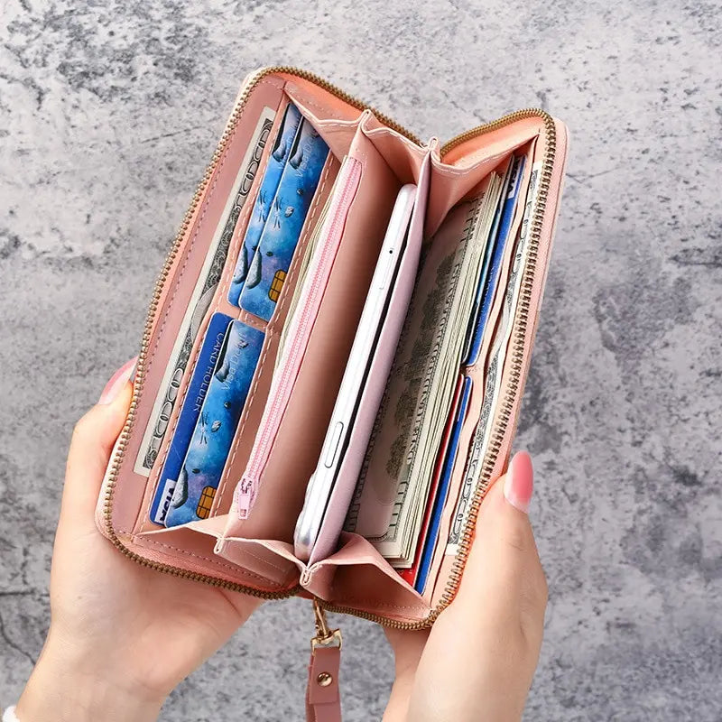 A hand holds an open pink fashion zipper wallet filled with various cards and cash.