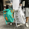 A person is holding a bright teal backpack and a white backpack, both featuring skateboard straps.