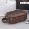 A brown leather travel cosmetic bag with a zipper and leather strap is shown next to a white sink.